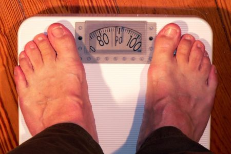 Ilustrasi timbangan dan tubuh manusia, menggambarkan konsep berfokus pada kesehatan nyata daripada sekadar angka berat badan