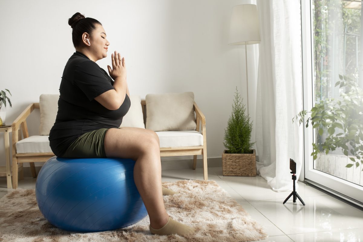 Seorang perempuan berolahraga di rumah sambil mengikuti instruktur fitness online, menggambarkan usaha menurunkan berat badan.